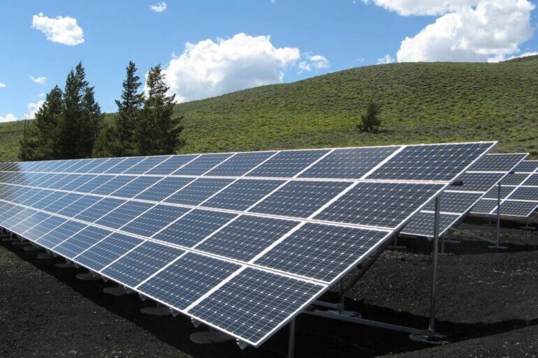 Imagem de um conjunto de painéis solares e ao fundo uma colina gramada.