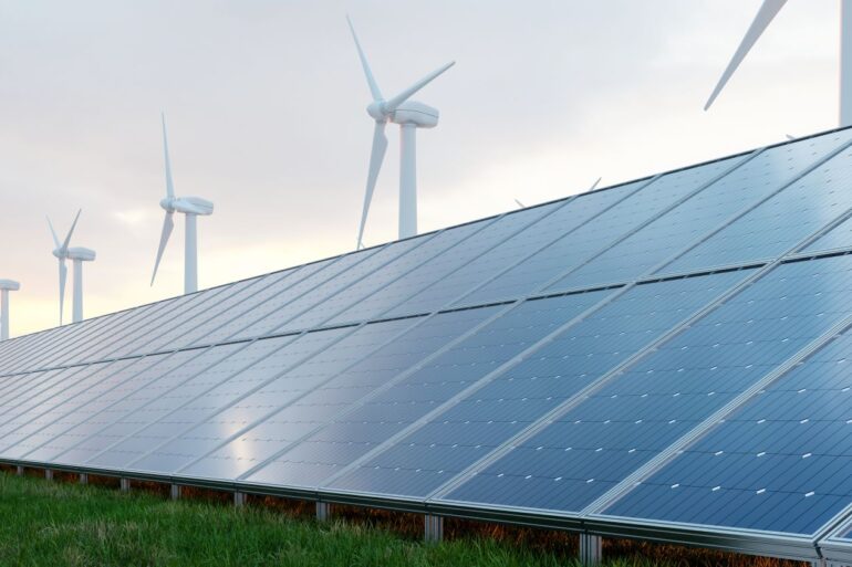 Painéis solares instalados sobre grama verde e turbinas eólicas atrás, para transição energética.