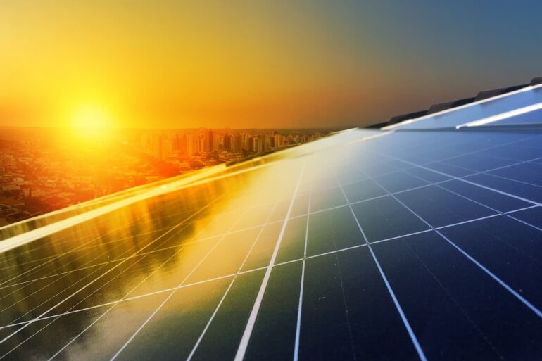 Painel solar com célula fotovoltaica em cima de telhado, com o sol se pondo e refletindo