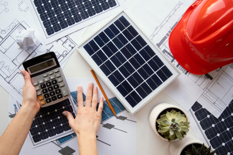 Projetos espalhados sob uma mesa com miniaturas de painéis solares e capacete de EPI, representando os cuidados na elaboração de projetos de energia solar.